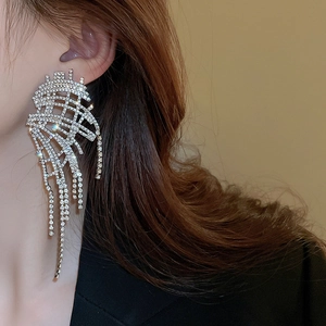 Detailed view of silver wing-shaped fringe earrings with rhinestones on a female model