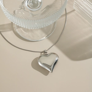 Dettaglio della collana con ciondolo a cuore vuoto argento e catena sottile su beige
