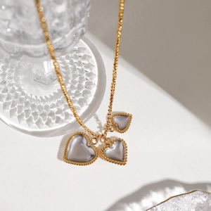 Two-tone stainless steel necklace featuring gold-edged heart pendants on a glass base