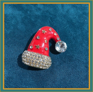 Detail of red enamel Christmas hat brooch with sparkling rhinestones and gold stars