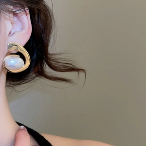 Close-up of elegant gold irregular curved earrings with white pearl inlay on model