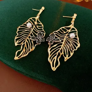 Elegant gold hollow leaf earrings with pearl and butterfly on green velvet display