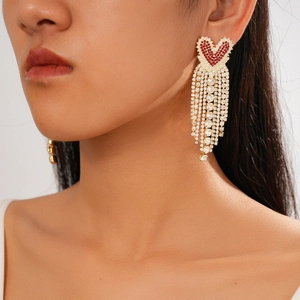 Close-up of heart-shaped gold earrings with red rhinestones and silver needle tassels