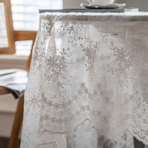 White lace tablecloth with floral embroidery draped on a table in a cozy room setting