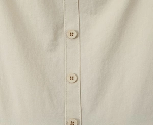 Makroaufnahme der beigen Baumwolltextur und der runden Vierlochknöpfe an einem Sommerkleid