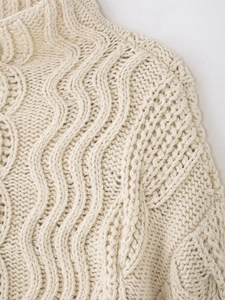 Close-up of cream cable-knit pattern and thick wool texture on a chunky sweater