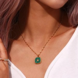 Detail of gold necklace with square green shell pendant and star engraving on model