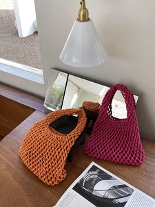 Detail of hand-woven orange and magenta mesh tote bags on a rustic wooden table