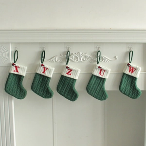 Green knitted Christmas stockings with white cuffs and red embroidered letters on a mantel