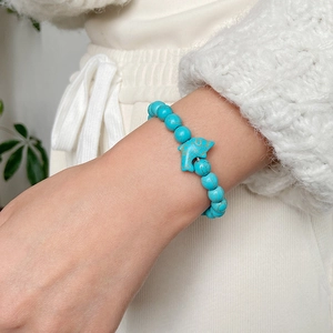 Close-up of blue turquoise beaded bracelet featuring a silver dolphin charm on wrist