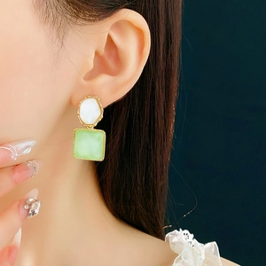 Detailansicht goldener Ohrringe mit grünem Stein und weißem Schmuckstein am Model