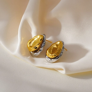 Détail de boucles d'oreilles bicolores irrégulières en métal liquide sur fond de soie