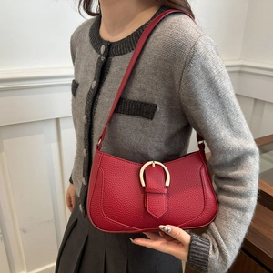 Detailed view of red pebble leather shoulder bag with gold horseshoe buckle on model