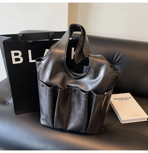 Detail of black faux leather tote bag with multi-pocket utility design on a sofa