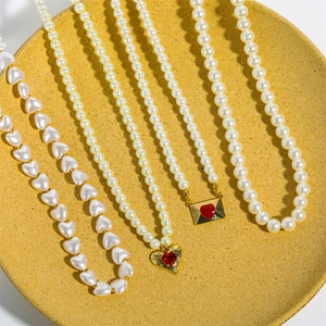 Detailed top view of 18K gold plated heart and envelope necklaces on yellow ceramic tray