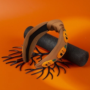 Detail of a brown fabric headband featuring three handmade beaded orange pumpkin patches