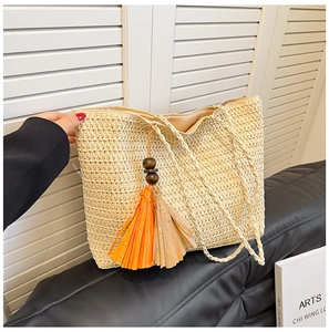 Close-up of woven straw tote bag featuring colorful tassels and wooden bead details