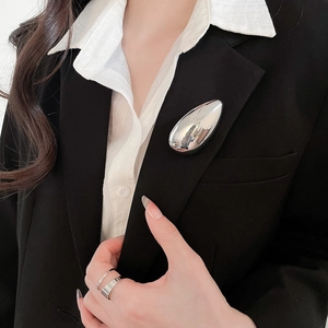 Close-up of liquid metal silver waterdrop brooch on black blazer with layered silver ring