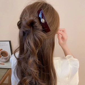 Detail of a vintage oval acrylic hair clip with a gold logo on a glossy dark brown finish