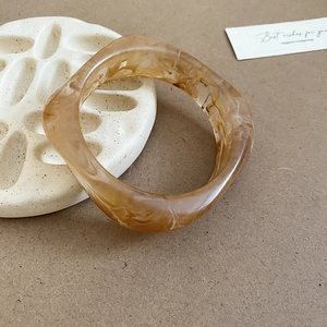 Detail of amber marble resin cuff bracelet with polished texture on a decorative tray