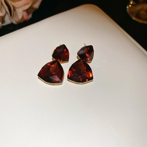 Macro shot of deep red geometric crystal earrings with gold plating on beige leather