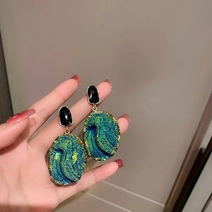Macro shot of retro drop oil resin earrings with blue-green texture and gold metal edges