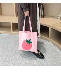 Pink canvas tote bag featuring a 3D plush strawberry embroidery held by a model