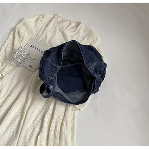 Détail à plat d'un sac à bandoulière en denim bleu marine sur une robe plissée blanche