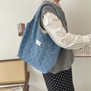 Grand sac cabas en denim bleu avec motifs de nœuds blancs porté à l'épaule pour le style