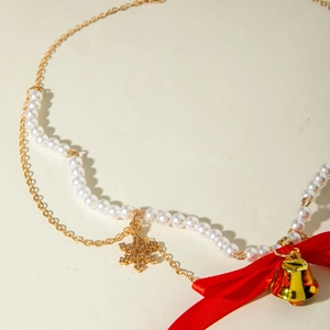 Detail of Christmas necklace with red ribbon bow, gold bell, and snowflake pendant