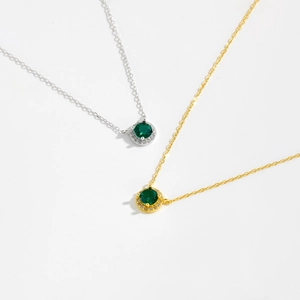 Detail of silver and gold necklaces featuring round green gemstones and zircon accents