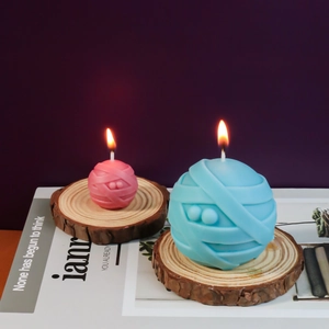 Details von zwei mumienförmigen Duftkerzen in Rosa und Blau auf Naturholzscheiben