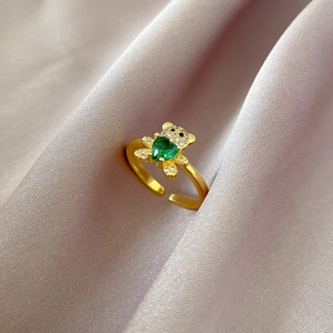 Macro detail of gold bear ring featuring green heart gem and zircon accents on satin
