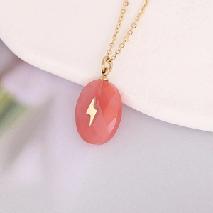 Macro shot of gold cross necklace with pink drop stone pendant and lightning pattern