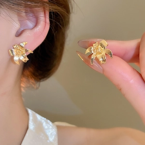 Detailed view of lily flower stud earrings in gold finish worn for size perspective