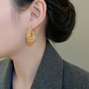 Boucles d'oreilles créoles torsadées plaquées or avec zircons portées par un mannequin