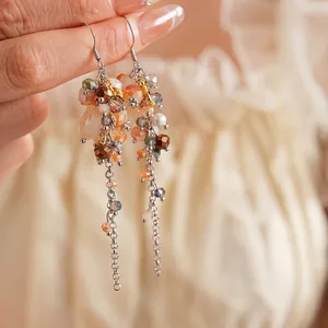 Vintage orange crystal and pearl tassel earrings with silver chains on fabric background