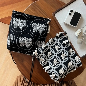 Detailed top view of embroidered black canvas crossbody bags on a wooden table surface
