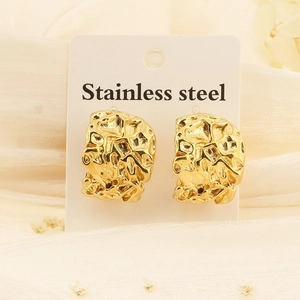 Macro shot of irregular C-shaped gold earrings with hammered lava texture on stainless steel