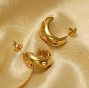 Détail de boucles d'oreilles créoles dorées avec zircons étoilés sur tissu en soie