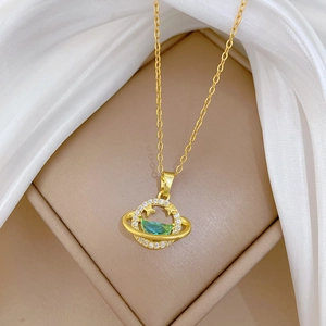 Detailed view of gold planet pendant with green gemstone and small diamonds on white silk