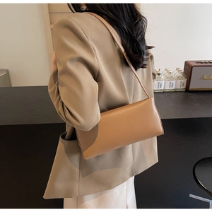 Side view of minimalist camel underarm baguette bag worn by model with tailored blazer