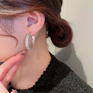 Close-up of silver C-hoop earring with woven texture and micro zircons on model