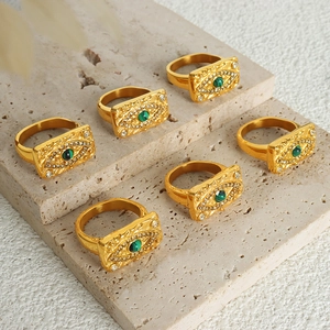 Gold evil eye rings with green gemstones and vintage texture on stone background