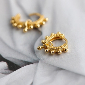 Macro shot of gold hoop earrings with bead detailing on a soft fabric background