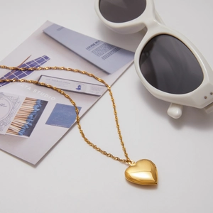 Detail of 18K gold-plated heart locket necklace with twist chain on a minimalist white setting