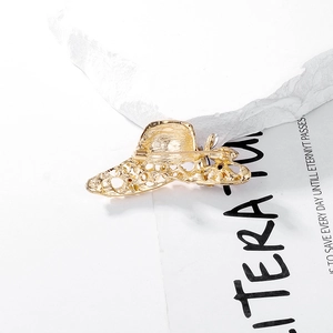 Elegant gold hat brooch with woven texture and pin clasp on white marble background