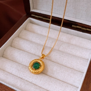 Detailed macro view of a vintage gold cross necklace with a green gem in a jewelry box