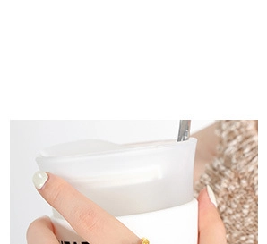 Dettaglio di una tazza in ceramica bianca con scritte nere, coperchio e cucchiaio