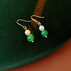 Dettaglio di orecchini vintage con perle e agata verde su un cuscino di velluto verde